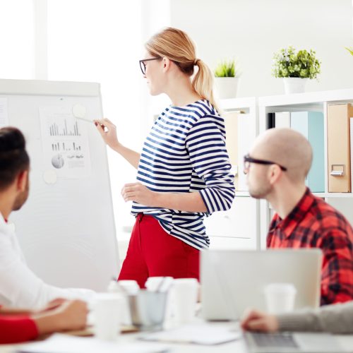 Business,Lady,Or,Teacher,Standing,By,Whiteboard,And,Pointing,At